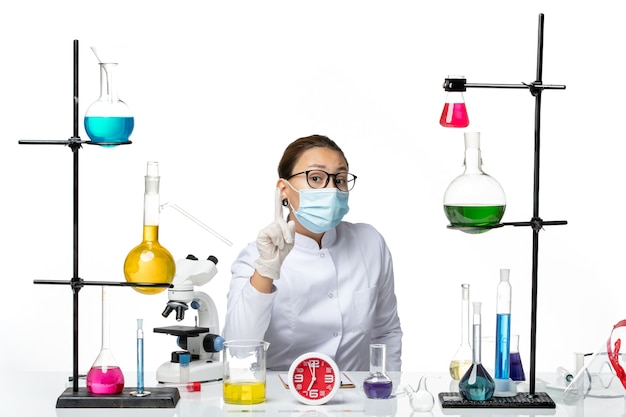Vue de face chimiste en combinaison médicale avec masque assis avec des solutions sur fond blanc clair virus de laboratoire de chimie covid- splash