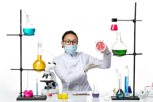 Vue de face chimiste en combinaison médicale avec masque tenant des horloges sur le fond blanc clair virus laboratoire chimie covid splash