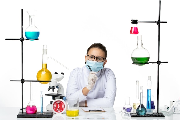 Vue de face chimiste en costume médical avec masque assis avec des solutions d'écriture de notes sur fond blanc clair splash laboratoire chimie virus covid