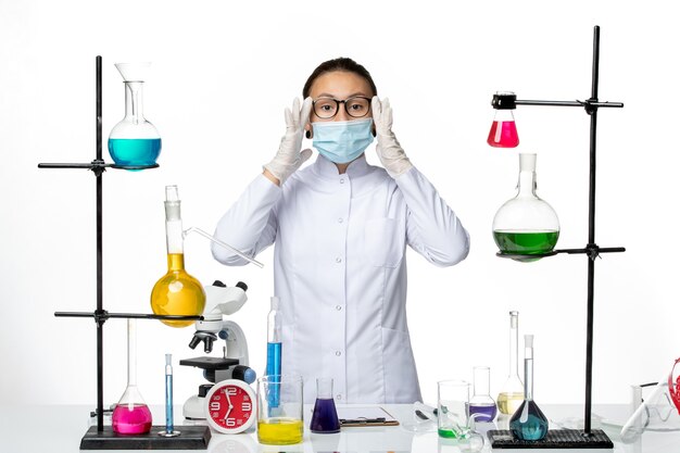 Vue de face chimiste en costume médical avec masque debout à l'intérieur de la salle avec des solutions sur fond blanc laboratoire de chimie de virus covid- splash