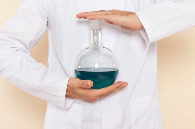 Vue de face chimiste masculin en costume spécial blanc tenant le ballon avec une solution bleue sur le mur de la crème chimie de l'expérience de laboratoire scientifique