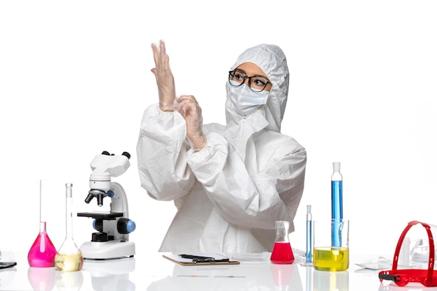 Vue de face chimiste en tenue de protection spéciale assis avec des solutions portant des gants sur fond blanc virus pandémique covid chimie