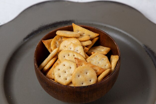 Vue de face des chips et des craquelins à l'intérieur de la plaque brune ronde à l'intérieur de la plaque grise