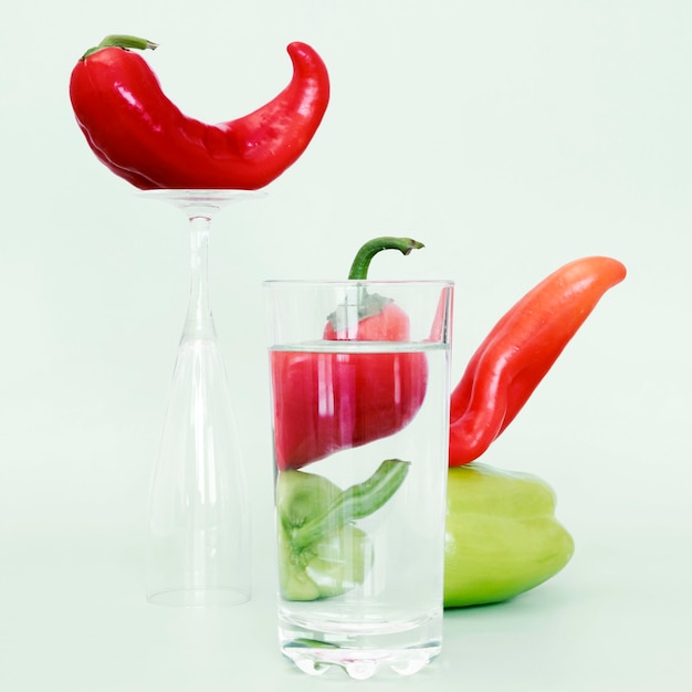 Photo gratuite vue de face de la cloche et des piments avec un verre d'eau