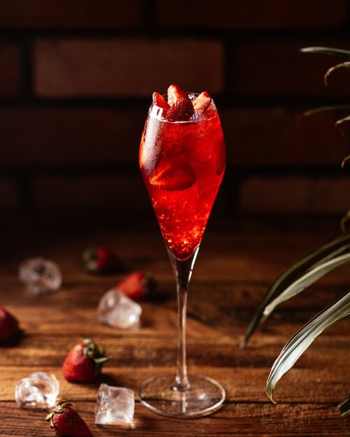 Une vue de face cocktail aux fraises avec des fruits frais et des glaçons sur la table cocktail de jus de fruits