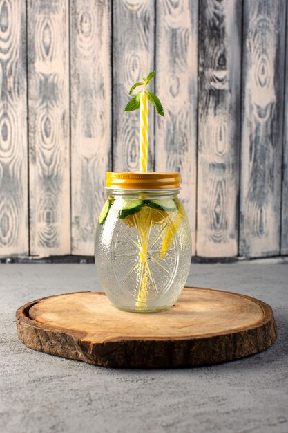 Une vue de face cocktail de citron boisson fraîche fraîche à l'intérieur de la coupe en verre citrons tranchés paille sur le bureau en bois et fond gris cocktail boisson fruit