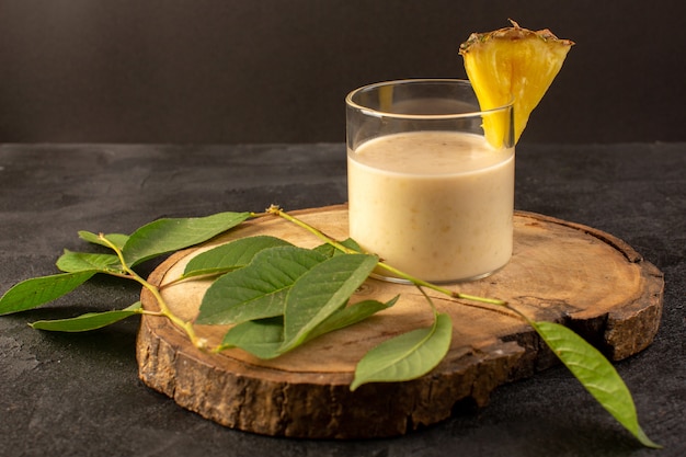 Une vue de face cocktail délicieux boisson rafraîchissante à l'intérieur du petit verre près d'un bureau en bois avec des feuilles vertes sur le fond sombre boire du jus d'été