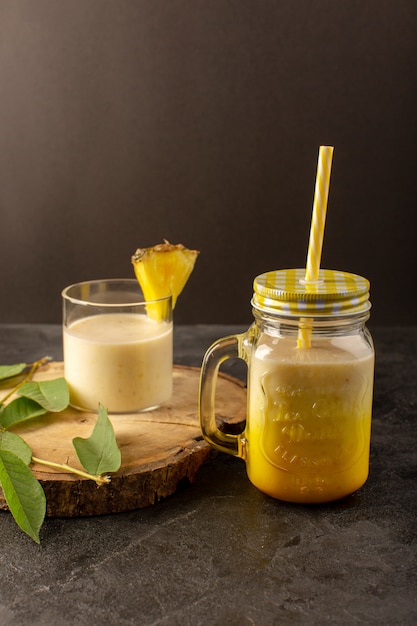 Une vue de face cocktail délicieux boisson rafraîchissante à l'intérieur peut avec de la paille près de bureau en bois le long des feuilles vertes sur le fond sombre boire du jus d'été
