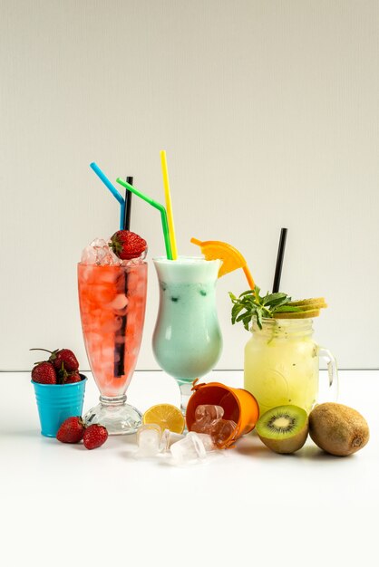 Une vue de face des cocktails froids frais à l'intérieur des verres avec des pailles avec des fruits frais isolés sur blanc