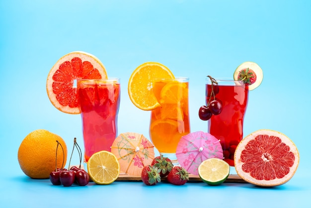 Une vue de face des cocktails de fruits frais avec des tranches de fruits frais refroidissement par glace sur bleu, boire du jus de fruits cocktail couleur de fruits