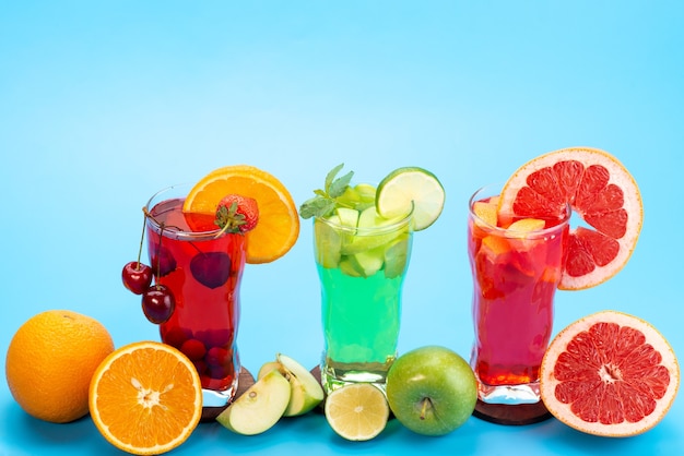 Une vue de face des cocktails de fruits frais avec des tranches de fruits frais refroidissement par glace sur bleu, boire du jus de fruits cocktail couleur de fruits