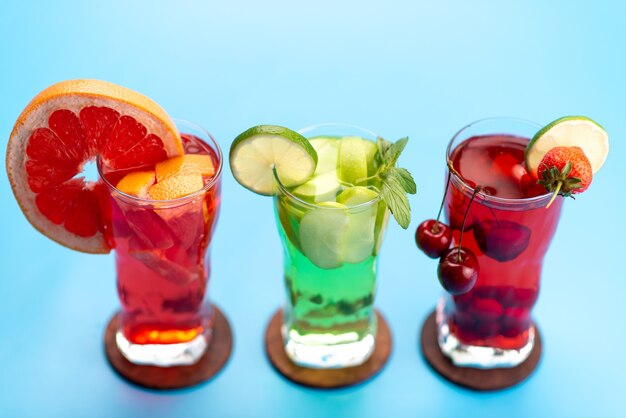 Une vue de face des cocktails de fruits frais avec des tranches de fruits frais refroidissement par glace sur bleu, boire du jus de fruits cocktail couleur de fruits