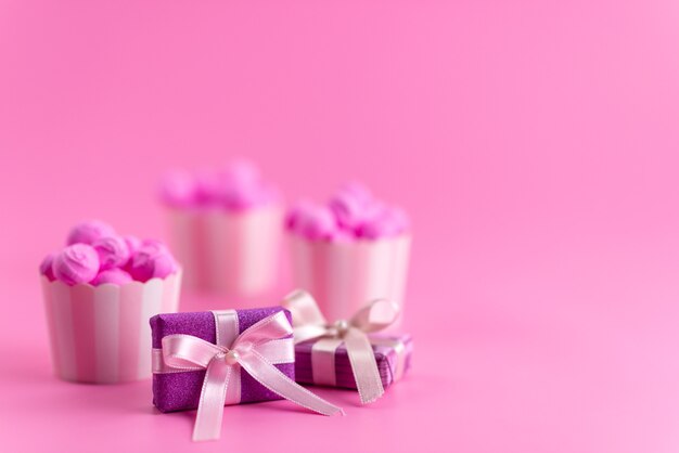 Une vue de face des coffrets cadeaux violets avec des bonbons roses sur un bureau rose