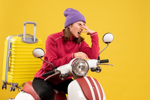 Vue de face en colère jeune fille sur un cyclomoteur avec valise jaune