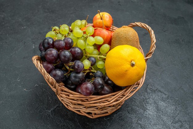Vue de face composition de différents fruits frais et mûrs à l'intérieur du panier sur fond gris foncé fruits frais moelleux santé mûrs