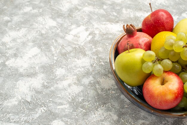 Vue de face de la composition de fruits frais pommes raisins et autres fruits sur le fond blanc fruits frais mûrs couleur mûre vitaminev