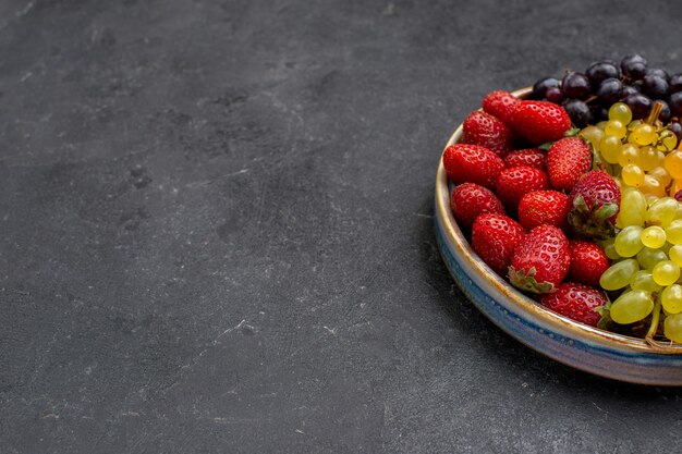 Vue de face de la composition des fruits fraises raisins framboises et mandarines sur un espace sombre