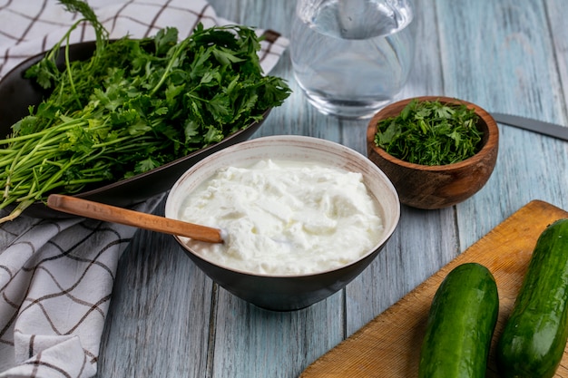 Vue de face des concombres sur une planche avec du yogourt et des verts sur une surface grise