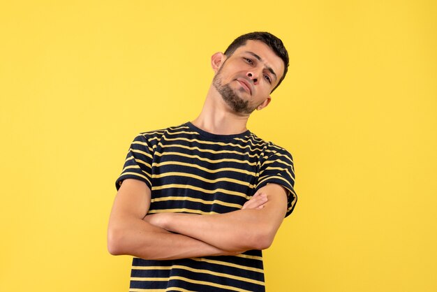 Vue de face confiant jeune homme en t-shirt rayé noir et blanc croisant les mains sur fond isolé jaune