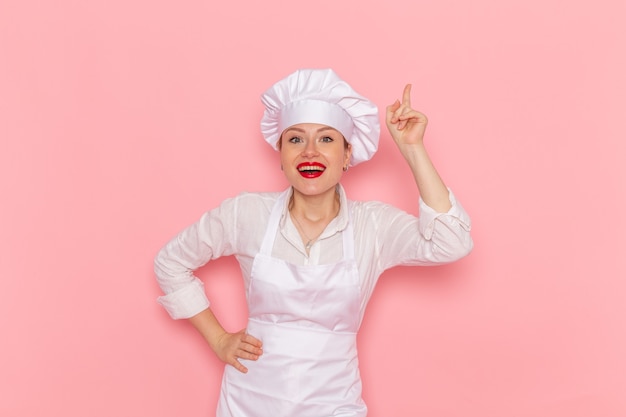 Vue de face confiseur femme en vêtements blancs posant avec une expression ravie sur la confiserie murale rose clair travail de pâtisserie douce