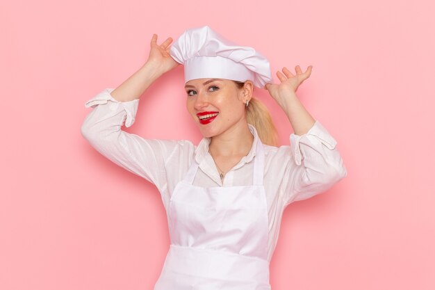 Vue de face confiseur femme en vêtements blancs souriant et posant sur le travail de travail de pâtisserie sucrée confiserie bureau rose clair