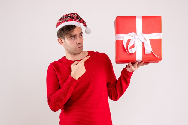 Vue de face confus jeune homme avec bonnet de Noel debout sur blanc