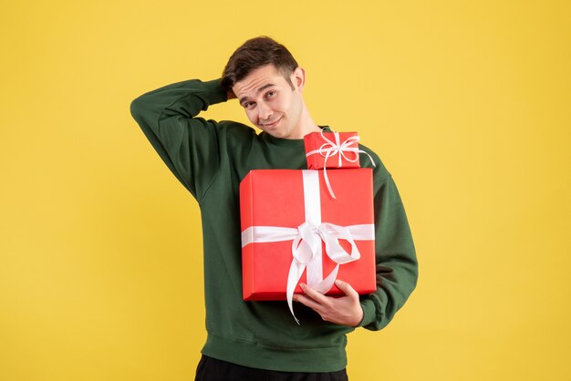 Vue de face confus jeune homme avec cadeau de Noël debout sur jaune