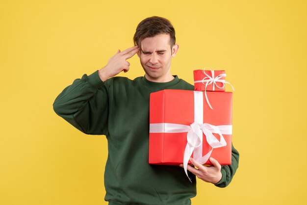 Vue de face confus jeune homme avec cadeau de Noël debout sur jaune