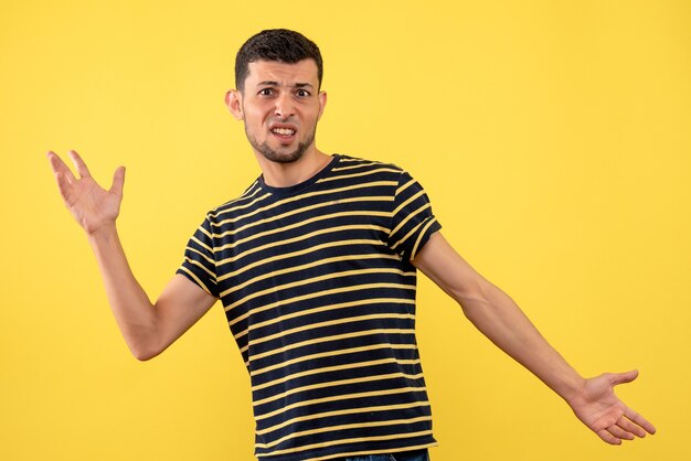 Vue de face confus jeune homme en t-shirt rayé noir et blanc fond isolé jaune