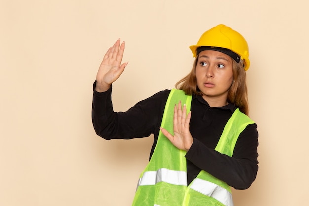 Vue de face constructeur féminin en casque jaune avec une expression prudente sur le mur blanc