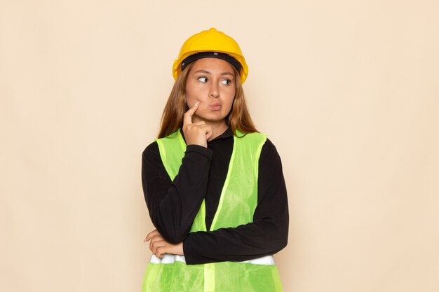 Vue de face constructeur féminin en chemise noire casque jaune posant la pensée sur le mur blanc