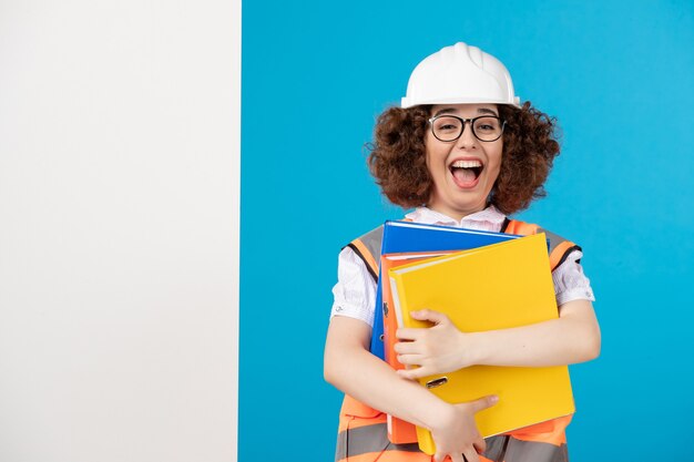 Vue de face constructeur féminin émotionnel en uniforme avec des documents sur bleu