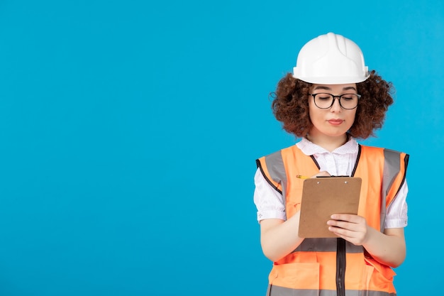 Vue de face constructeur féminin en uniforme d'écrire des notes sur bleu