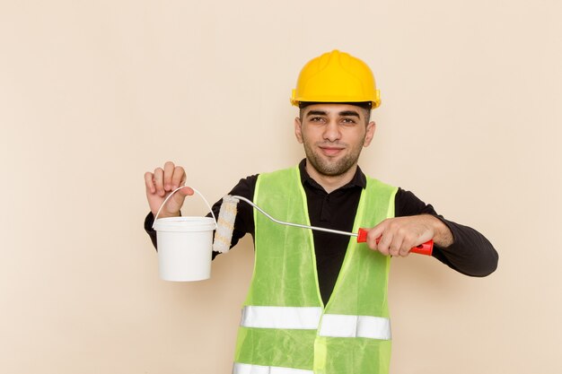 Vue de face constructeur masculin en casque jaune tenant de la peinture et posant sur un bureau léger