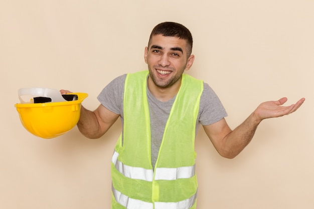 Vue de face constructeur masculin décoller casque jaune posant avec sourire sur fond clair