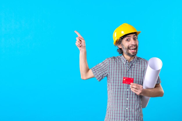 Vue de face constructeur masculin tenant le plan et la carte bancaire sur le bâtiment de l'argent de l'architecture du travail du constructeur de couleur de fond bleu