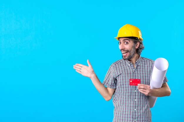 Vue de face constructeur masculin tenant un plan et une carte bancaire sur fond bleu argent design constructeur architecture bâtiment travail casque couleurs de travail