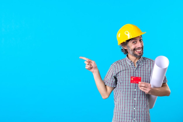 Vue de face constructeur masculin tenant un plan et une carte bancaire sur fond bleu design constructeur architecture bâtiment couleur de travail