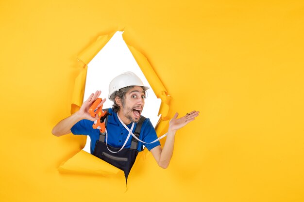 Vue de face constructeur masculin en uniforme avec appareil sur mur jaune bâtiment travailleur architecture couleur travail constructeur travail
