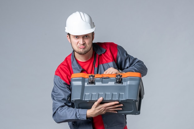 vue de face constructeur masculin en uniforme essayant d'ouvrir la boîte à outils sur fond gris