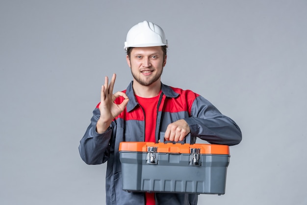 Photo gratuite vue de face constructeur masculin en uniforme et étui à outils tenant un casque sur fond gris