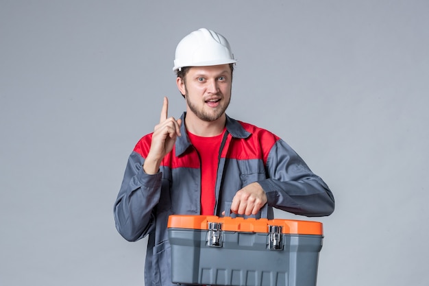 vue de face constructeur masculin en uniforme et étui à outils tenant un casque sur fond gris