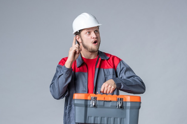 vue de face constructeur masculin en uniforme et étui à outils tenant un casque sur fond gris