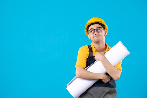 Vue de face constructeur masculin en uniforme avec plan papier sur bleu