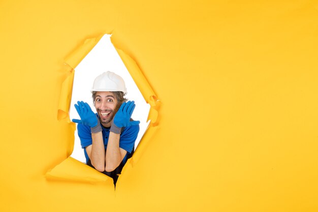 Vue de face constructeur masculin en uniforme souriant sur un mur jaune homme de construction couleur constructeur architecture papier travailleur