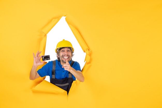 Vue de face constructeur masculin en uniforme tenant une carte bancaire noire sur fond jaune