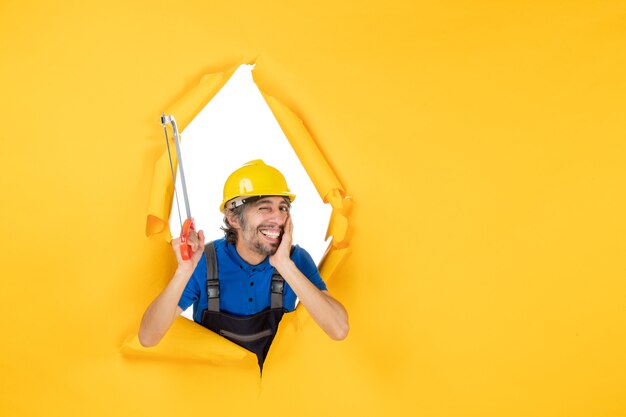 Vue de face constructeur masculin en uniforme tenant une scie à archet sur fond jaune