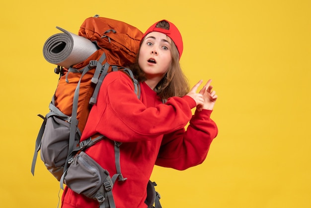 Vue de face cool femme voyageur avec sac à dos pointant les doigts derrière