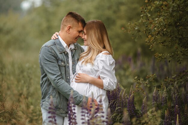 Vue de face d'un couple caucasien juste marié attendant un bébé, s'embrassant presque dans un pré avec des fleurs de lupin