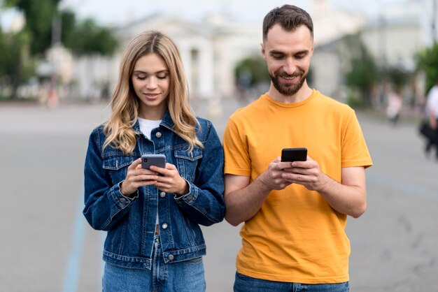 Vue de face couple heureux à l'aide de leurs téléphones mobiles